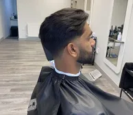 A low taper fade with a shaped beard, seen from the side in the chair